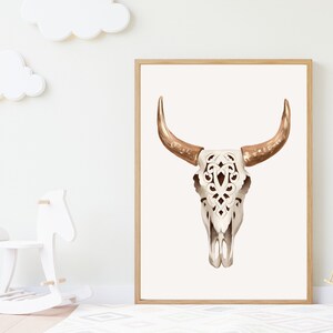May include: A framed print featuring a watercolor illustration of a bull skull. The skull is white with intricate cut-out designs, and the horns are a warm, metallic gold color. The artwork is displayed in a light wood frame.