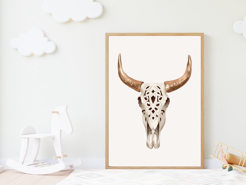 May include: A framed print featuring a watercolor illustration of a bull skull. The skull is white with intricate cut-out designs, and the horns are a warm, metallic gold color. The artwork is displayed in a light wood frame.