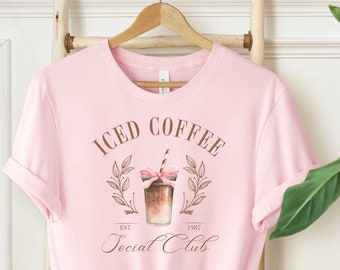 May include: Pink t-shirt with a graphic of a mason jar filled with iced coffee and the text "Iced Coffee Social Club Est. 1987".