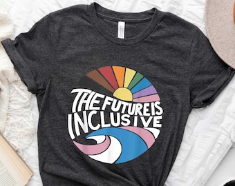 Puede incluir: Una camiseta gris oscuro con un diseño gráfico colorido que dice "The Future is Inclusive". El gráfico presenta un círculo arcoíris con un sol y una ola.