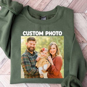 Puede incluir: Una sudadera verde oliva con una foto familiar rectangular. La foto, centrada en el frente, muestra a un hombre, una mujer y un beb&eacute;. El texto blanco "CUSTOM PHOTO" est&aacute; encima de la foto.