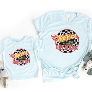May include: Two light blue t-shirts with a Hot Wheels logo and text that says "Hot Mess, A Little Stressed, Boy Mama" on the larger shirt and "Hot Mess, Never Stressed, Mama's Boy" on the smaller shirt.
