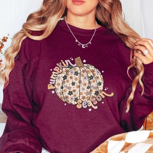 May include: A maroon sweatshirt with a floral pumpkin design and the text "Pumpkin Season" in a retro font.