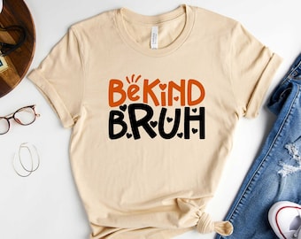 May include: A beige t-shirt with the text "Be Kind BRUH" in orange and black lettering with small black hearts around the text.