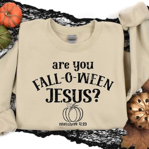 May include: A beige sweatshirt with the text "Are you Fall-o-Ween Jesus?" and a small pumpkin graphic. The text "Matthew 11:19" is printed below the pumpkin.