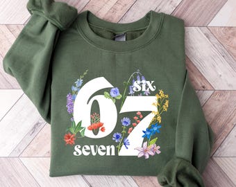 May include: An olive green sweatshirt with the numbers "07" in white, and the word "seven" below. The numbers and text are surrounded by a floral design with colourful flowers. The word "six" is above the number "0".