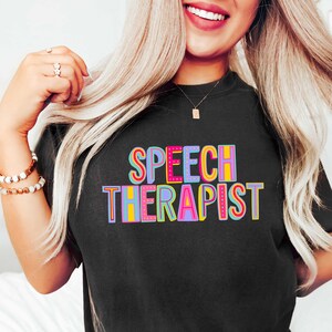 May include: Black t-shirt with the text "SPEECH THERAPIST" in colorful letters.