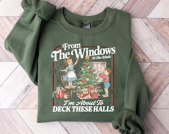 May include: Green sweatshirt with a festive graphic. The graphic features a vintage illustration of children decorating a Christmas tree, with the text "From The Windows To The Walls, I'm About To Deck These Halls."
