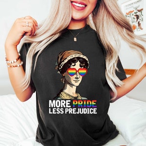 May include: Black t-shirt featuring a graphic of a woman wearing rainbow heart-shaped sunglasses and the text "More Pride Less Prejudice".