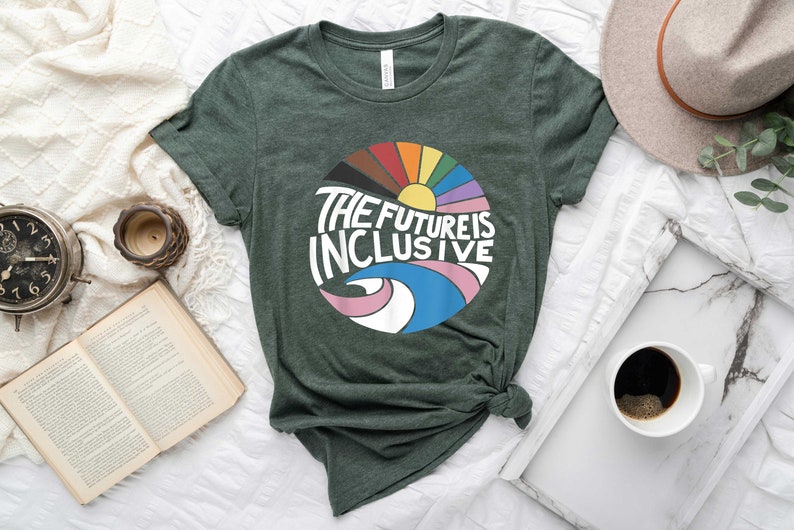 May include: A dark green t-shirt with a colorful graphic design of a rainbow circle with a sun and the text "The Future is Inclusive".