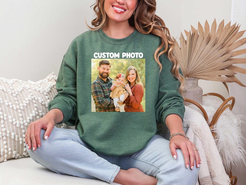 Puede incluir: Sudadera verde con una foto familiar impresa en la parte delantera. La foto muestra a una familia de tres. El texto "CUSTOM PHOTO" est&aacute; impreso encima de la foto en un rect&aacute;ngulo blanco. La persona de la imagen lleva vaqueros azul claro.