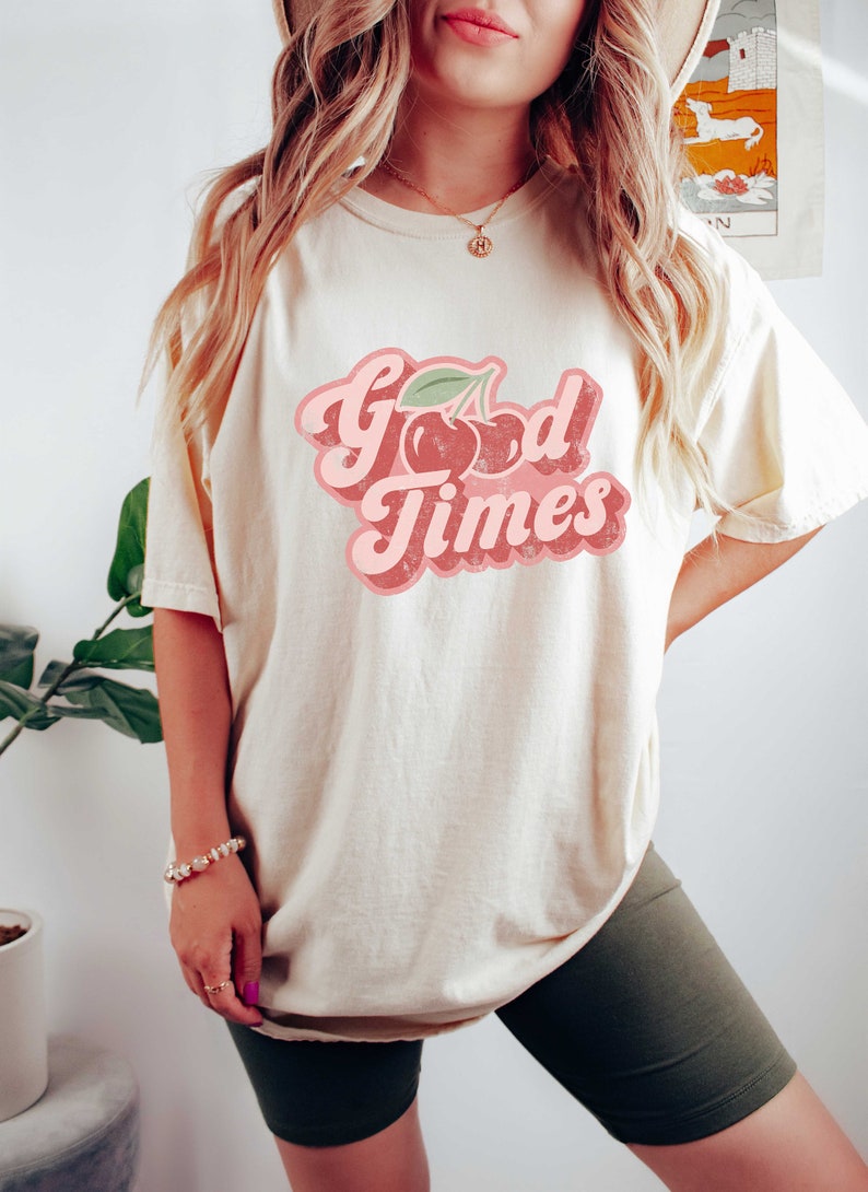 Pu&ograve; includere: T-shirt color crema con la scritta "Good Times" in un font retr&ograve;, con una grafica di ciliegie. La maglietta ha una vestibilit&agrave; ampia e il design &egrave; nei toni del rosa e del rosso.