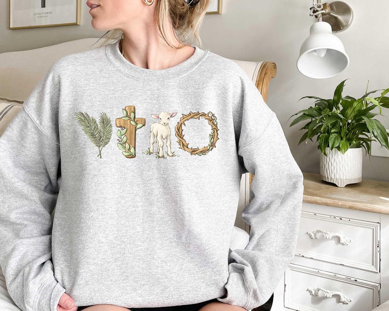 May include: A gray sweatshirt with a graphic design of a cross, a lamb, a palm branch, and a crown of thorns. The design is in shades of brown, green, and white.