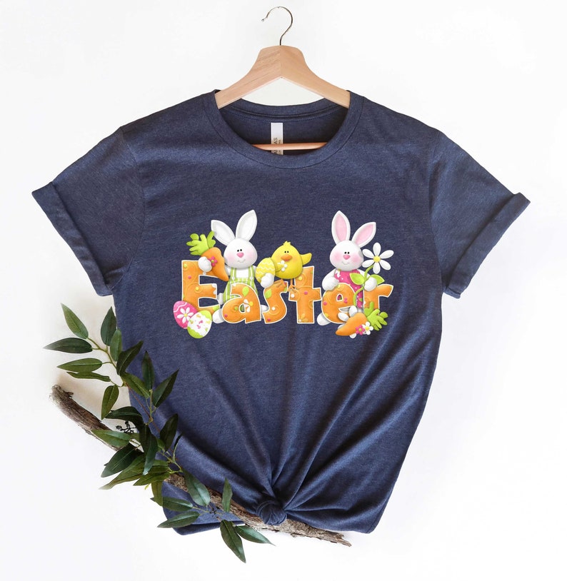 May include: A navy blue t-shirt with a graphic of two bunnies and a chick holding carrots and an Easter egg. The word "Easter" is spelled out in orange letters with green and yellow accents.