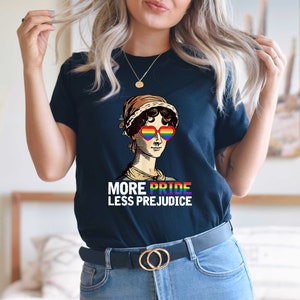 May include: A navy blue t-shirt featuring a graphic of a woman wearing rainbow heart-shaped sunglasses and the text "More Pride Less Prejudice".