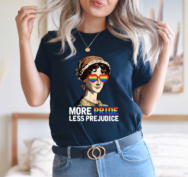 May include: A navy blue t-shirt featuring a graphic of a woman wearing rainbow heart-shaped sunglasses and the text "More Pride Less Prejudice".