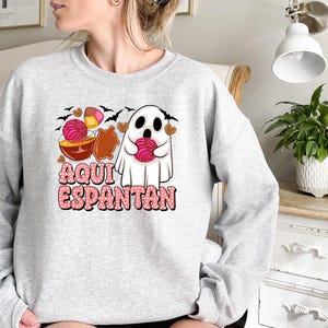 May include: Grey sweatshirt featuring a ghost holding a pink sweet and the text "Aqui Espantan" in pink lettering.
