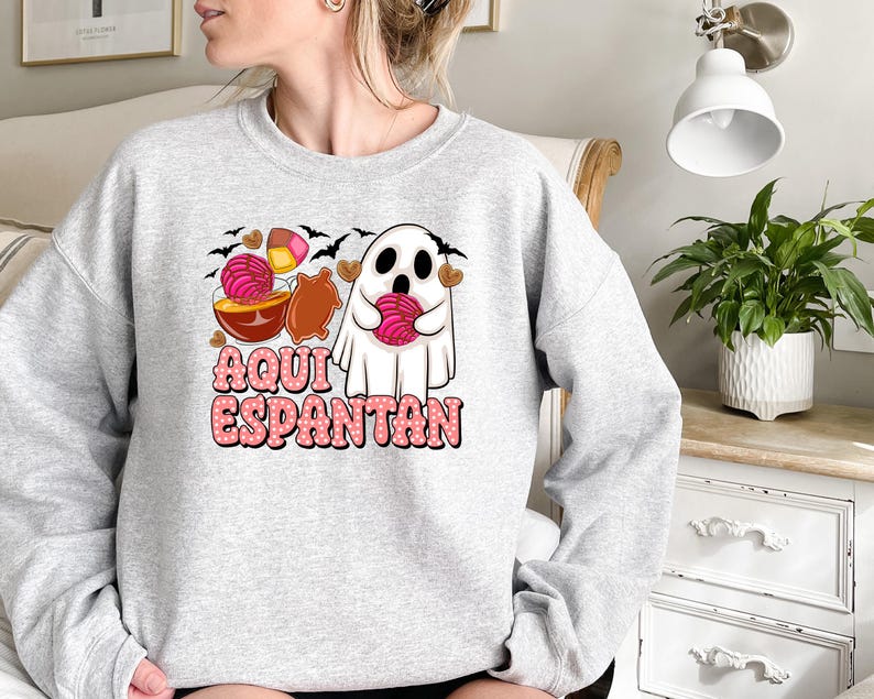 May include: Grey sweatshirt featuring a ghost holding a pink sweet and the text "Aqui Espantan" in pink lettering.