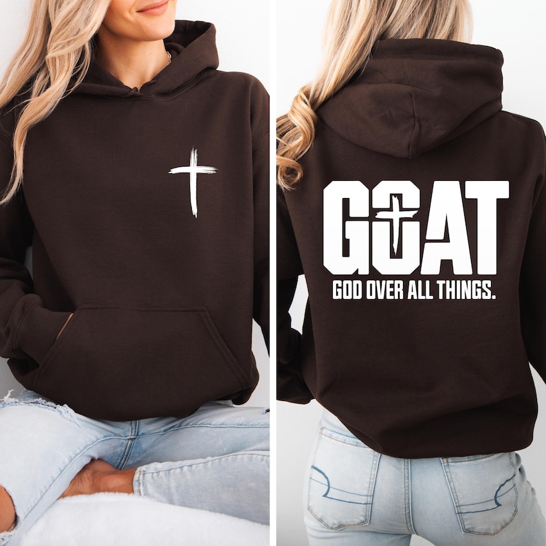 Pode incluir: Um moletom marrom escuro com uma cruz branca na frente e a palavra "GOAT" com uma cruz no "O" nas costas. O texto "GOD OVER ALL THINGS" est&aacute; abaixo da palavra "GOAT".