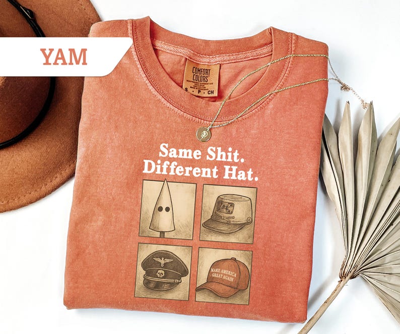 Peut inclure: Un t-shirt corail avec le texte "Same Shit. Different Hat." et quatre illustrations de chapeaux. Un collier en or et un chapeau marron sont &eacute;galement visibles. Le t-shirt est de Comfort Colors.