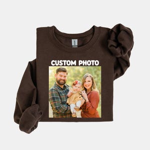 Puede incluir: Una sudadera marr&oacute;n oscuro con una foto familiar impresa en la parte delantera. La foto muestra a un hombre, una mujer y un beb&eacute;. El texto "CUSTOM PHOTO" est&aacute; impreso en blanco encima de la foto.