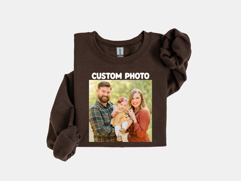 Puede incluir: Una sudadera marr&oacute;n oscuro con una foto familiar impresa en la parte delantera. La foto muestra a un hombre, una mujer y un beb&eacute;. El texto "CUSTOM PHOTO" est&aacute; impreso en blanco encima de la foto.