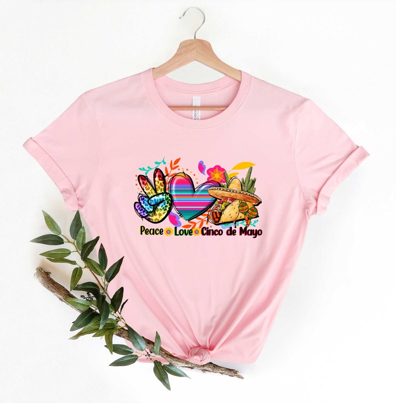 Puede incluir: Camiseta rosa con un signo de paz, un coraz&oacute;n y un sombrero con el texto "Peace Love Cinco de Mayo".