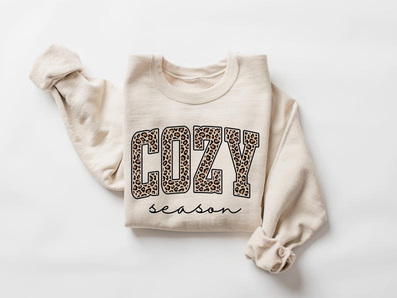 Pu&ograve; includere: Felpa color crema con le parole "COZY season" stampate sul davanti. La parola "COZY" &egrave; in grandi lettere con un motivo leopardato. La parola "season" &egrave; in corsivo.