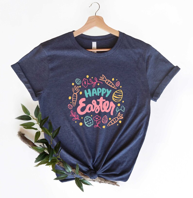May include: A navy blue t-shirt with a colorful graphic design that says "Happy Easter" surrounded by images of carrots, eggs, and flowers.