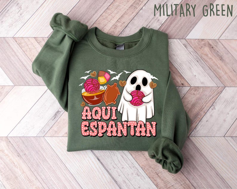 May include: A green sweatshirt featuring a ghost holding a pink pastry and the text "Aqui Espantan" in pink lettering.