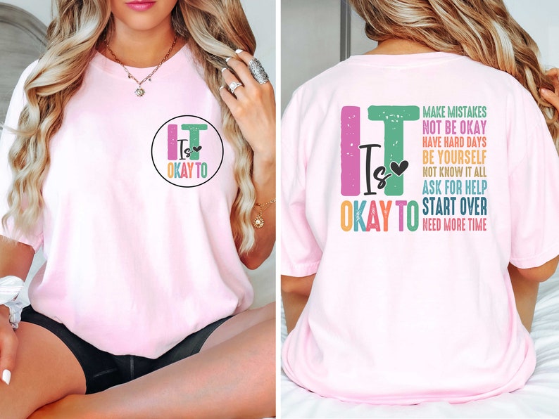Pode incluir: Camiseta rosa com o texto "It is okay to" em um c&iacute;rculo na frente e o mesmo texto com as palavras "make mistakes, not be okay, have hard days, be yourself, not know it all, ask for help, start over, need more time" nas costas.