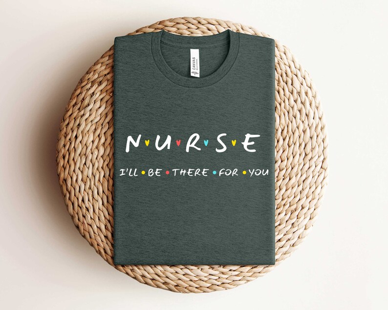 Puede incluir: Camiseta gris oscuro con el texto "NURSE" en letras de colores con corazones entre cada letra. El texto "I'll be there for you" est&aacute; impreso en negro debajo.
