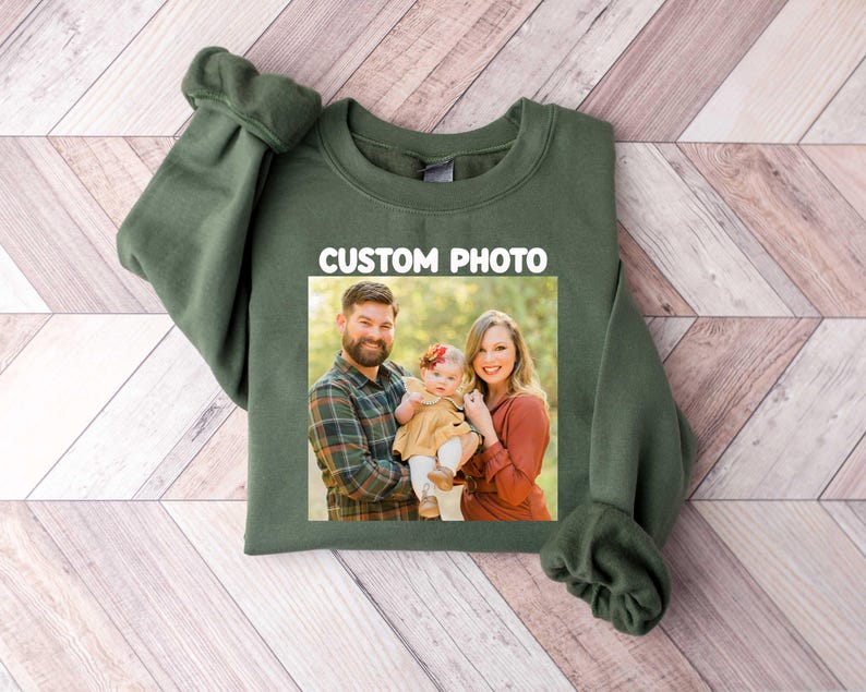 Puede incluir: Una sudadera verde oliva con una foto familiar rectangular. La foto, centrada en el frente, muestra a un hombre, una mujer y un beb&eacute;. El texto blanco "CUSTOM PHOTO" est&aacute; encima de la foto.