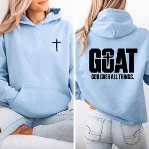 Pode incluir: Moletom azul claro com bolso frontal e uma cruz preta na frente. A parte de tr&aacute;s do moletom apresenta a palavra "GOAT" com uma cruz e o texto "GOD OVER ALL THINGS."