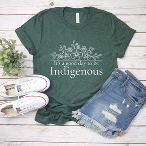 May include: A green t-shirt with a white floral design and the text "It's a good day to be Indigenous".