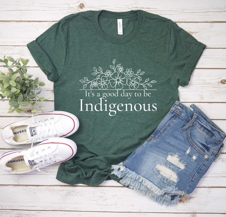 May include: A green t-shirt with a white floral design and the text "It's a good day to be Indigenous".