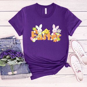 May include: Purple t-shirt with a graphic of two white bunnies and a yellow chick with the word "Easter" in orange letters.