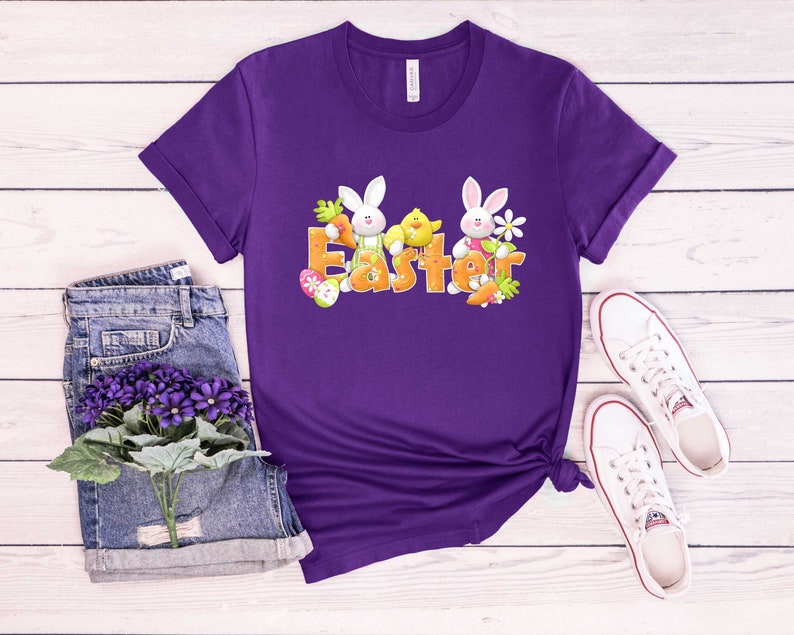 May include: Purple t-shirt with a graphic of two white bunnies and a yellow chick with the word "Easter" in orange letters.