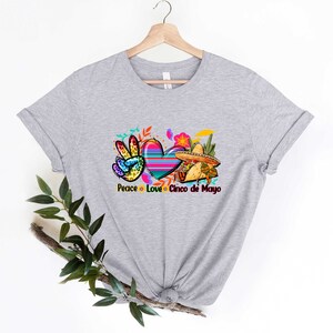 Puede incluir: Camiseta gris con un signo de paz, un coraz&oacute;n y un sombrero con el texto "Peace Love Cinco de Mayo".