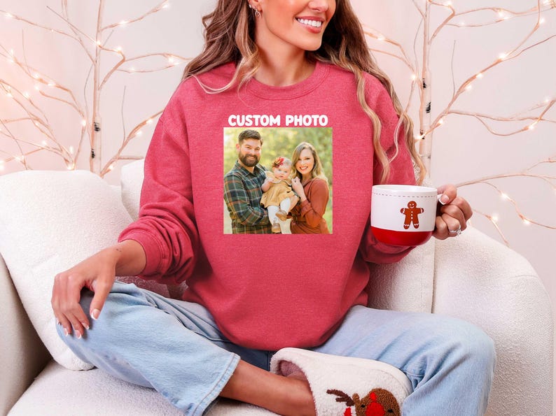 Puede incluir: Una sudadera roja con una foto familiar y el texto "CUSTOM PHOTO". La persona sostiene una taza blanca y roja con un dise&ntilde;o de hombre de jengibre. La persona lleva vaqueros azules y zapatillas de reno.