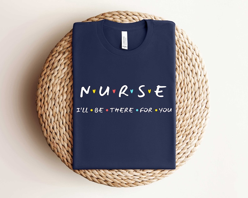 Puede incluir: Camiseta azul marino con el texto "NURSE" en letras de colores con corazones entre cada letra. El texto "I'll be there for you" est&aacute; impreso en negro debajo.
