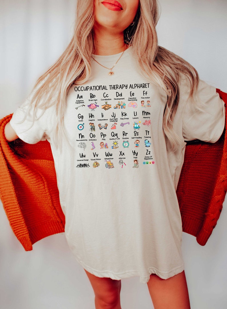 May include: A white t-shirt with a graphic of an occupational therapy alphabet. The alphabet is illustrated with icons representing different aspects of occupational therapy, such as adaptive equipment, brain gym, coordination, development, executive functioning, fine motor, goals, helpful, independence, just right challenge, key group, leisure, memory, neurodiversity,  orthodontics, play, quality of life, routine, self-feeding, toileting, universal design, visual motor, wheelchair, exercise, yoga, and zones of regulation.