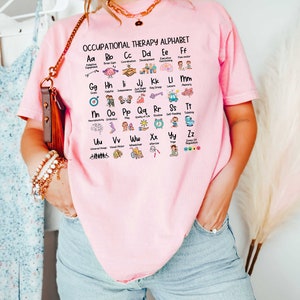 May include: A pink t-shirt with the text "Occupational Therapy Alphabet" and a graphic of the alphabet with icons representing different occupational therapy concepts.