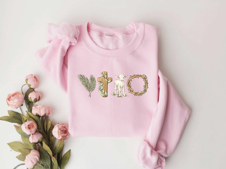 May include: Pink sweatshirt with a graphic design of a cross, a lamb, and a crown of thorns. The graphic is in shades of brown, green, and white.