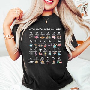 May include: Black t-shirt with a white graphic of an occupational therapy alphabet. Each letter is paired with an image and a word related to occupational therapy. For example, "Aa" is paired with "Adaptive Equipment" and an image of a wheelchair.