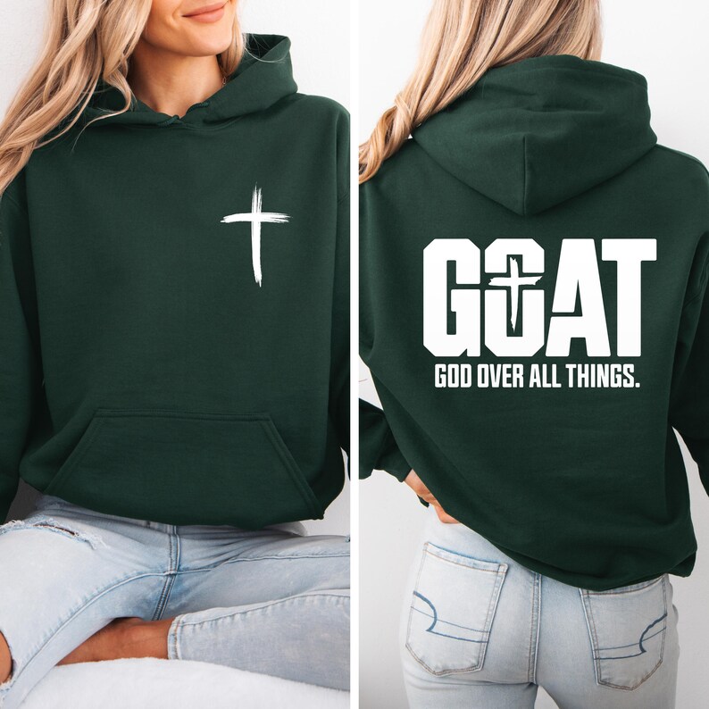 Pode incluir: Moletom verde escuro com uma cruz branca na frente e o texto "GOAT GOD OVER ALL THINGS" nas costas. O moletom tem um bolso frontal e um capuz. O texto e a cruz est&atilde;o em negrito branco.