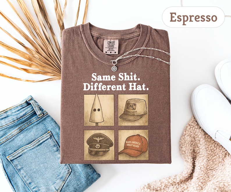 Peut inclure: T-shirt couleur expresso avec le texte "Same Shit. Different Hat." et des illustrations de diff&eacute;rents chapeaux. Un collier argent&eacute; et des baskets blanches sont &eacute;galement visibles. Le t-shirt est pr&eacute;sent&eacute; avec un jean bleu et une plante s&eacute;ch&eacute;e.