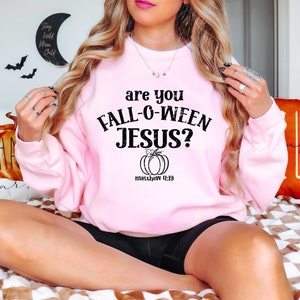 May include: A pink sweatshirt with the text "are you FALL-O-WEEN JESUS?" and a small pumpkin graphic with the text "matthew 11:19" underneath.