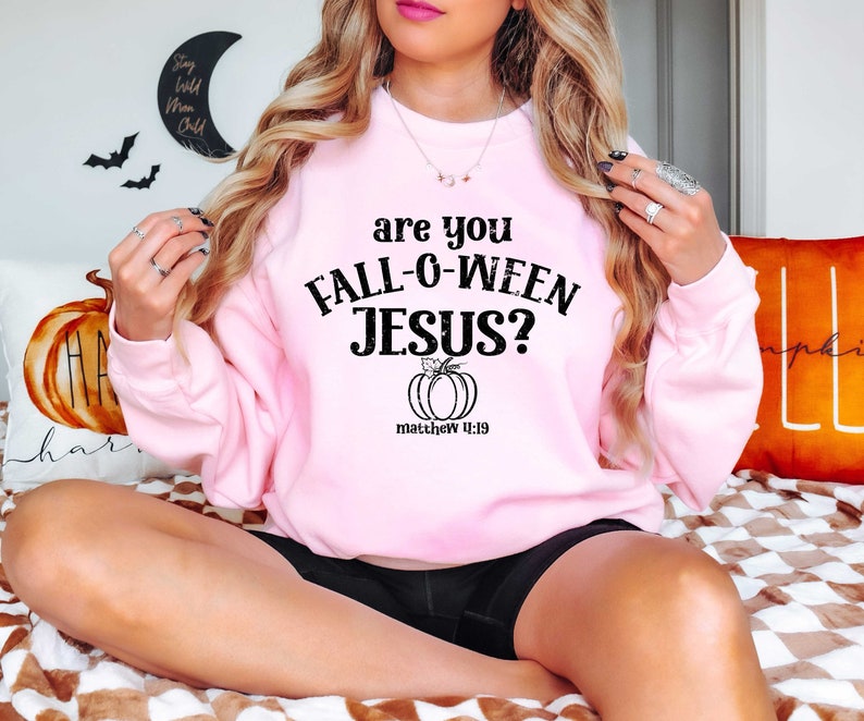 May include: A pink sweatshirt with the text "are you FALL-O-WEEN JESUS?" and a small pumpkin graphic with the text "matthew 11:19" underneath.