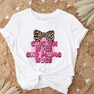 May include: White t-shirt with a pink bow and the text "Chicken Nugs and Mama Hugs" in pink.